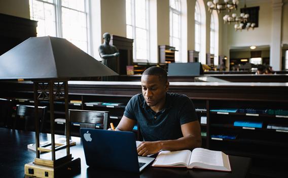 Student studying at a table with book and laptop in the Matheson Reading Room