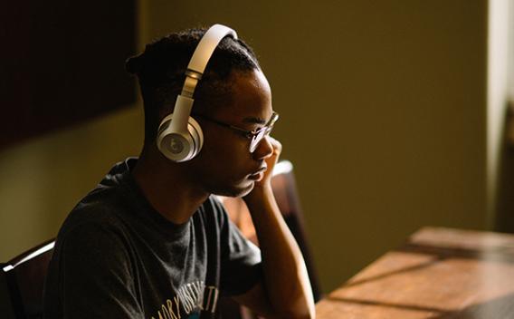 A student with headphones in the Matheson Reading Room, with late afternoon light