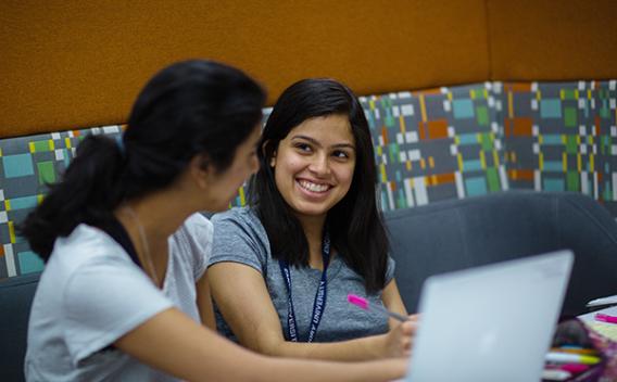 Two students with laptops, laughing in a study room located in Woodruff Library