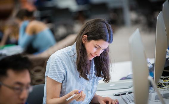 Student writing with a pen at a desktop computer