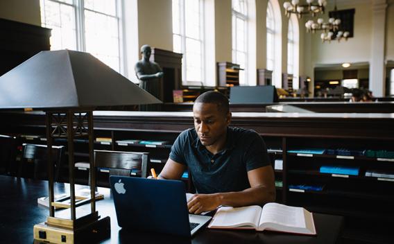 Student studying at a table with book and laptop in the Matheson Reading Room