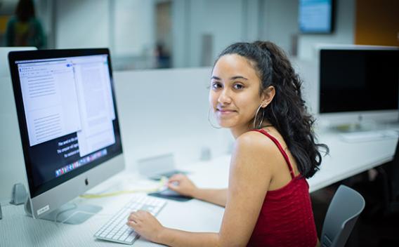 Student at desktop computer, smiling at the camera