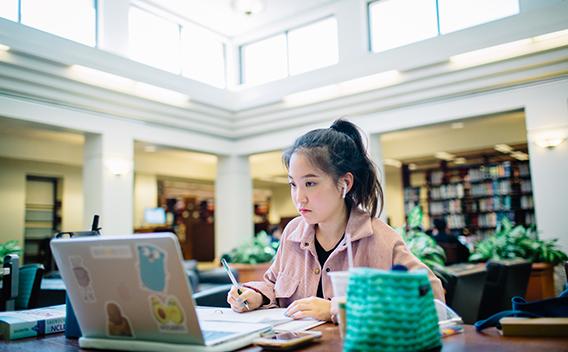 Student watching a class on her laptop and taking notes