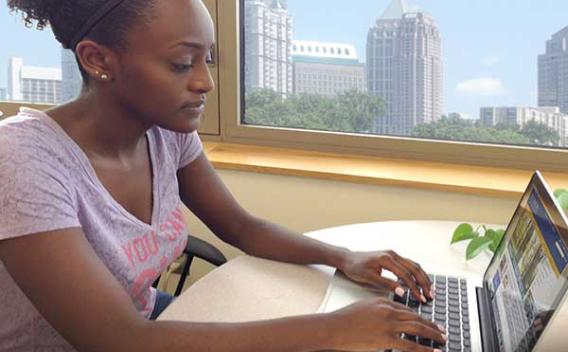 Young woman searching a laptop for open educational resources by a window showing sunny buildings