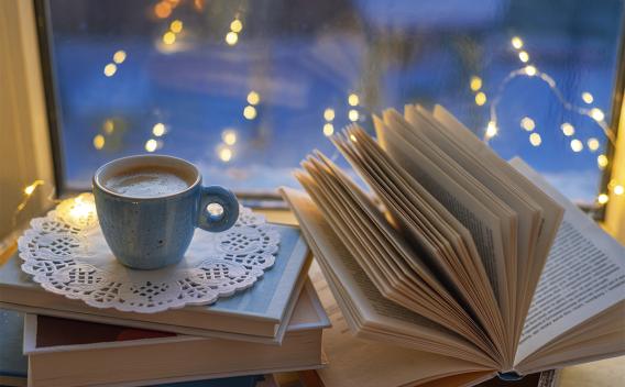 Cozy scene of book, coffee, holiday lights, and snow